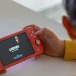 Child holding a pink handheld game console while a digital game loads on the screen.