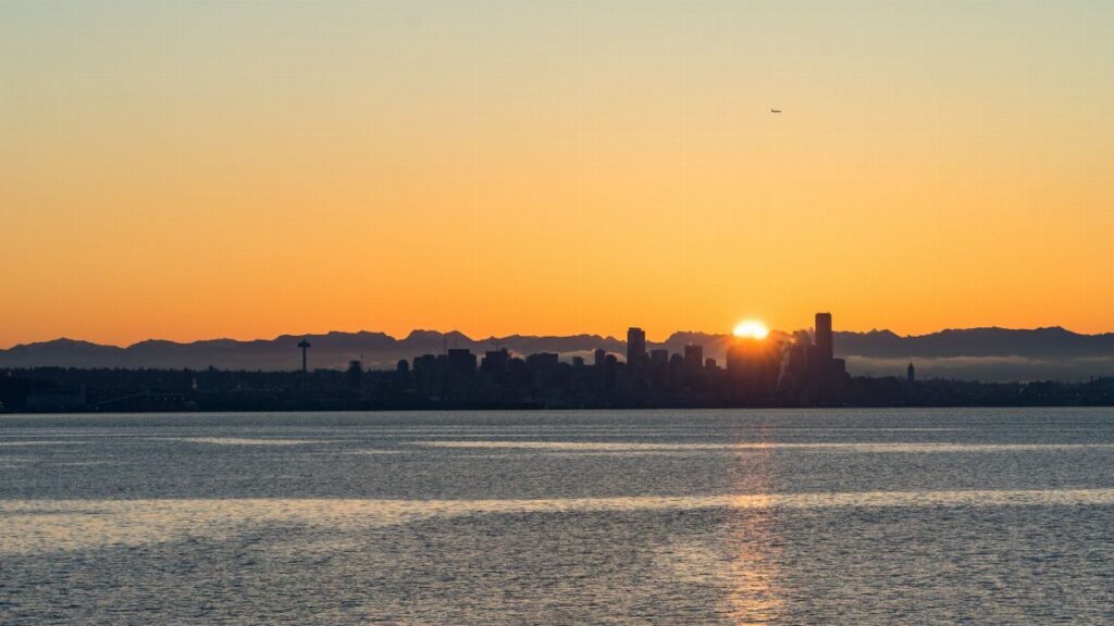 Breathtaking view of Seattle skyline at sunset with vibrant orange hues over calm waters.