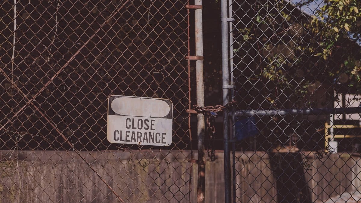 A rusty chain link fence with a 'Close Clearance' sign indicating security and safety measures.