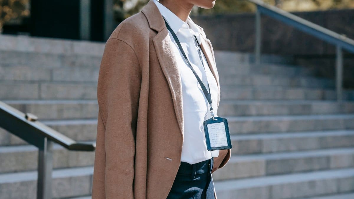 Side view of crop anonymous African American female entrepreneur with badge in classy brown coat standing near stairs with metal railings