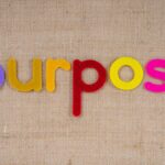 Colorful felt letters spelling 'purpose' on a textured fabric background with ample copyspace.