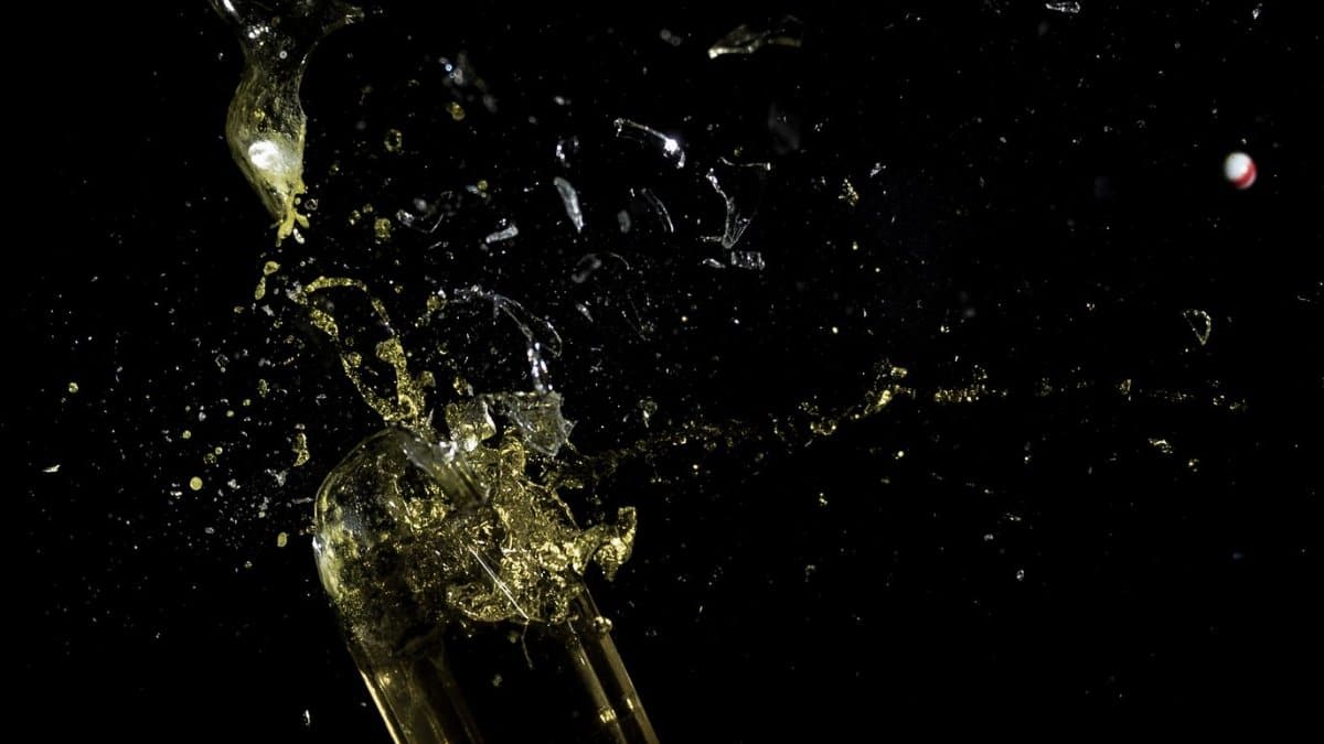 High-speed capture of a glass bottle shattering against a black background.
