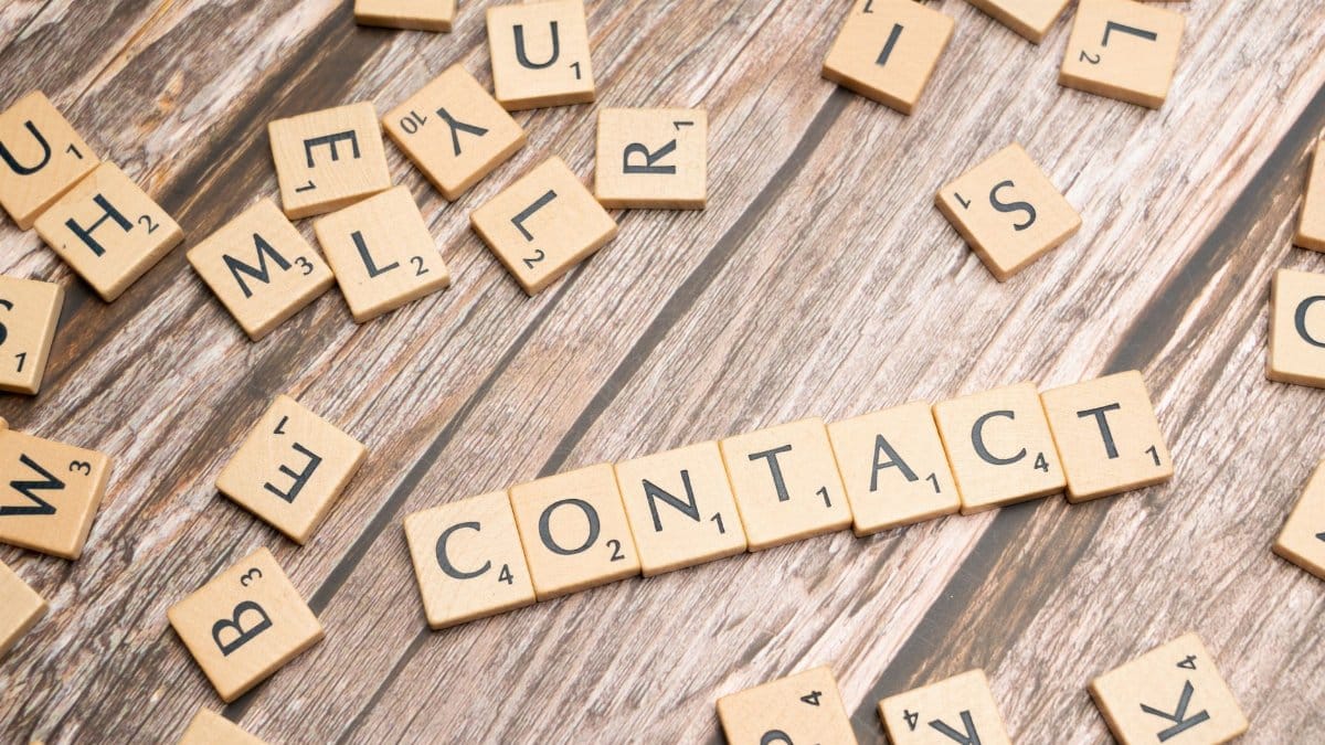 Scrabble-style letter tiles spelling 'contact' on wooden surface.