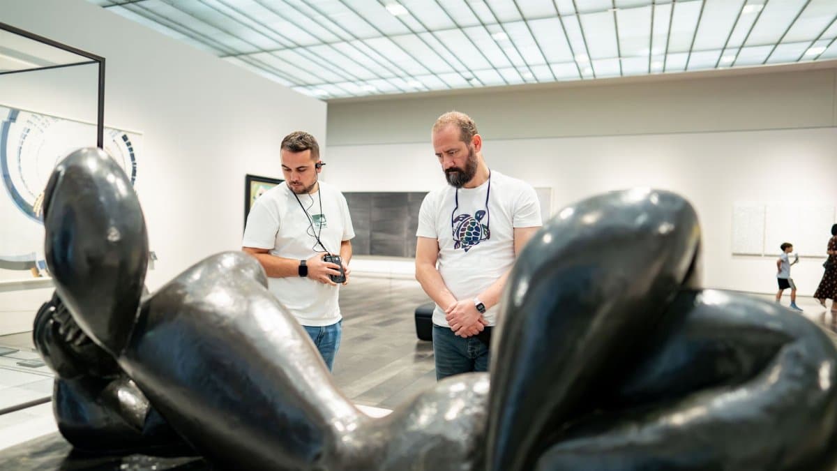 Two men observe a modern sculpture in a gallery setting, showcasing art appreciation.