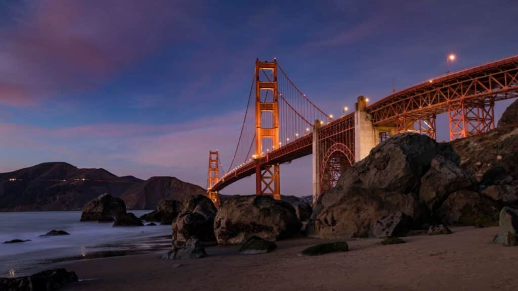 Scenic view of the Golden Gate Bridge at twilight with rocky beach foreground.