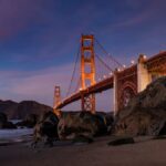 Scenic view of the Golden Gate Bridge at twilight with rocky beach foreground.