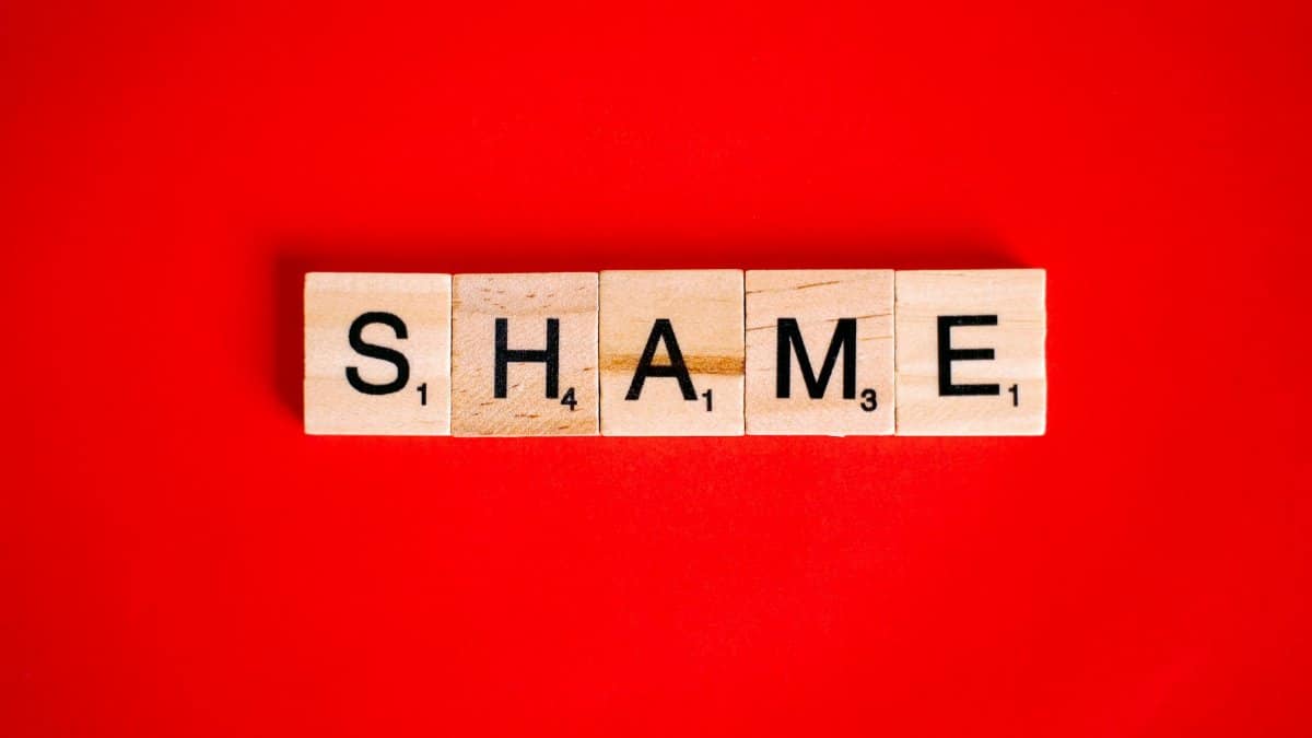 Scrabble tiles spelling the word 'Shame' on a vibrant red backdrop.