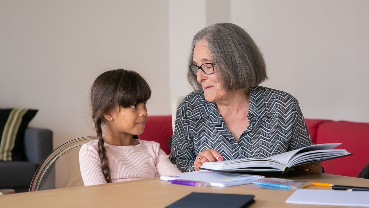 An elderly woman and a young girl sharing a book indoors, fostering a bond through reading.