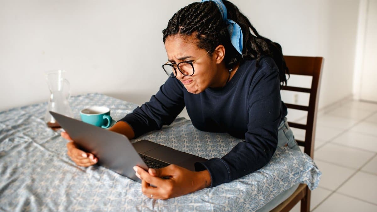 A young woman expressing frustration while using a laptop at home.