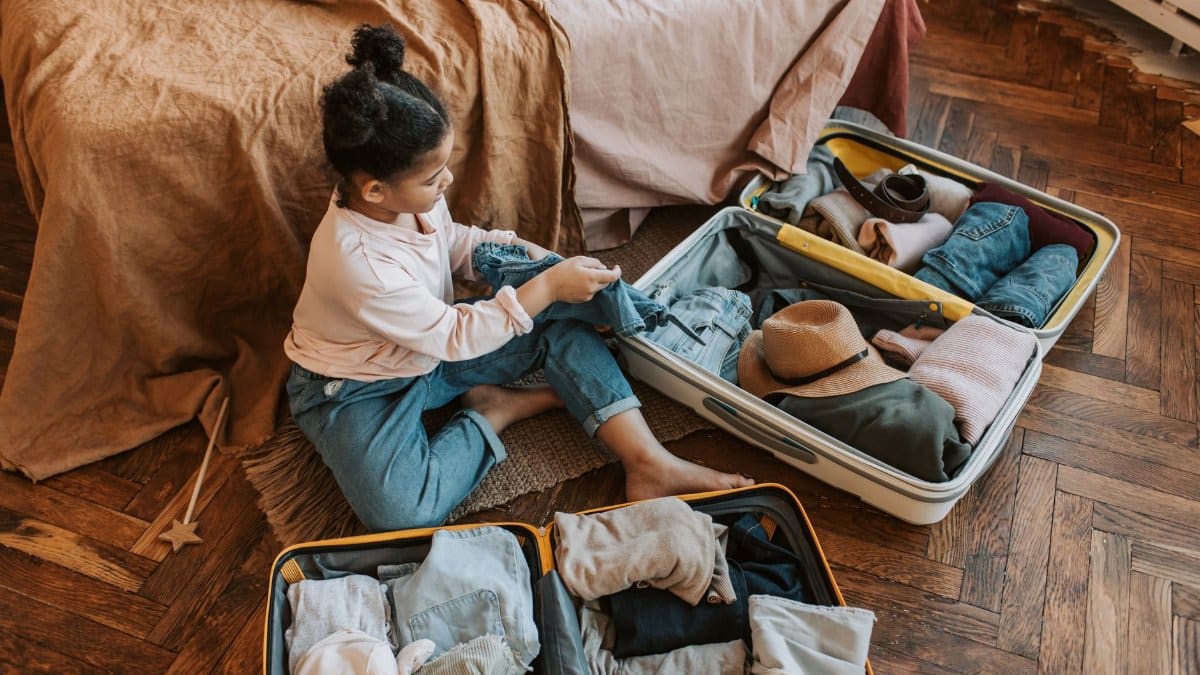 Young child sitting on bed packing a suitcase for an upcoming family vacation.