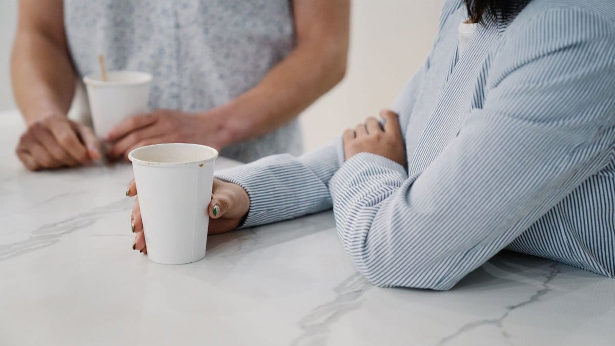 Two people conversing over coffee cups in a modern office setting, promoting a casual work atmosphere.