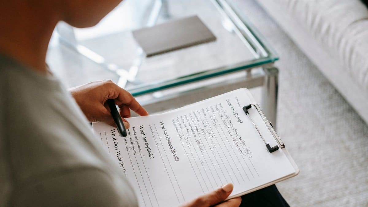 From above of blurred anonymous female psychologist reading documents on clipboard while sitting in office near table during session