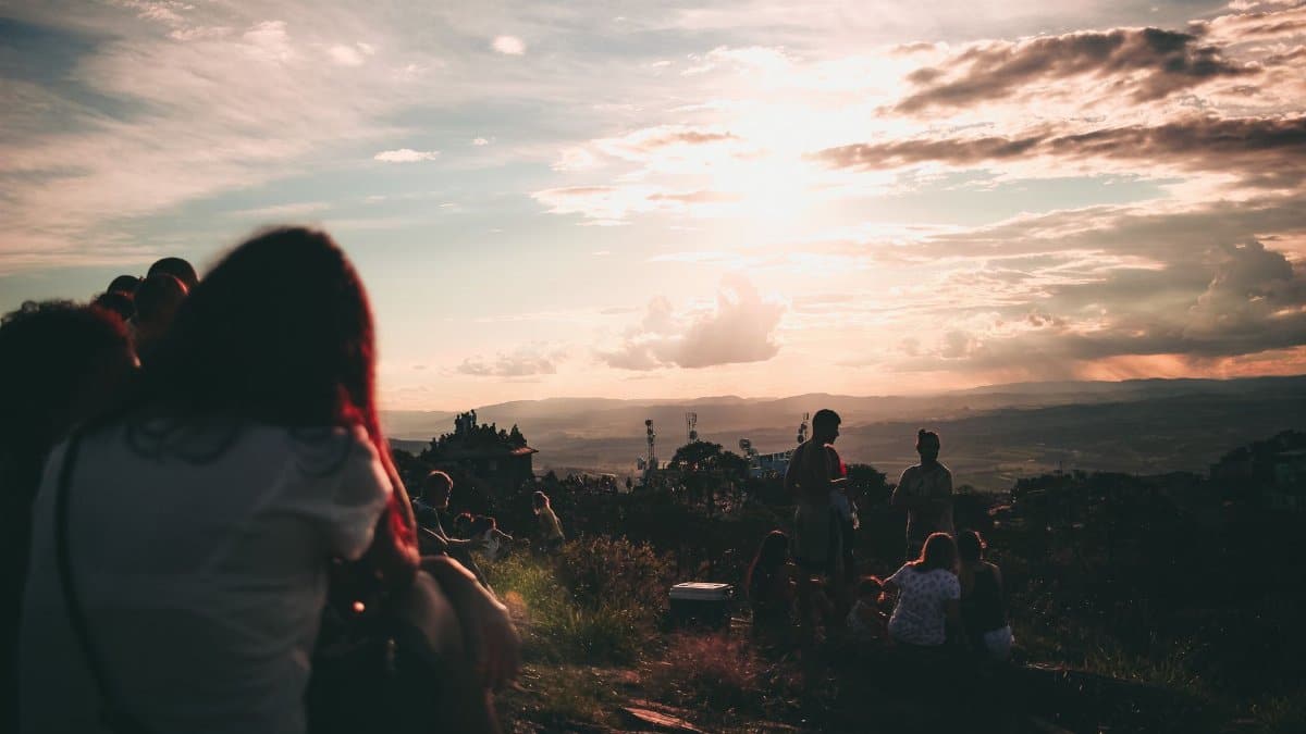 Silhouette of a group of friends relaxing on a hill overlooking a scenic sunset.