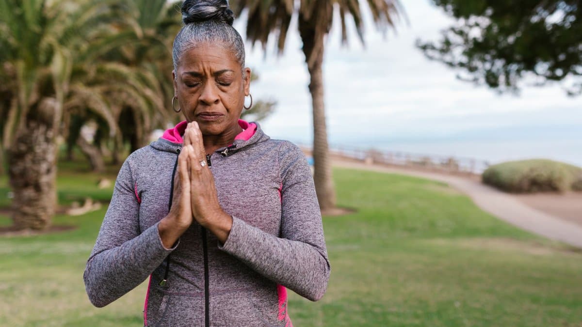 Elderly woman meditating outdoors in a park, promoting health and relaxation.