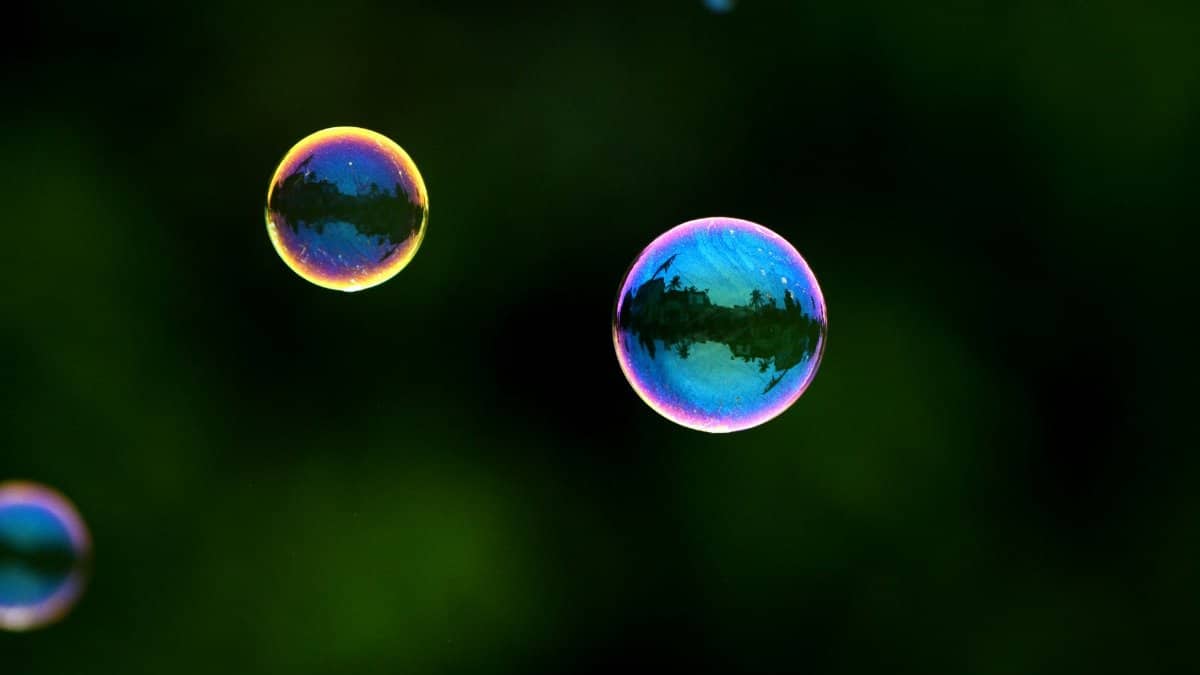 Colorful soap bubbles with reflections floating against a dark green backdrop, creating a mesmerizing effect.