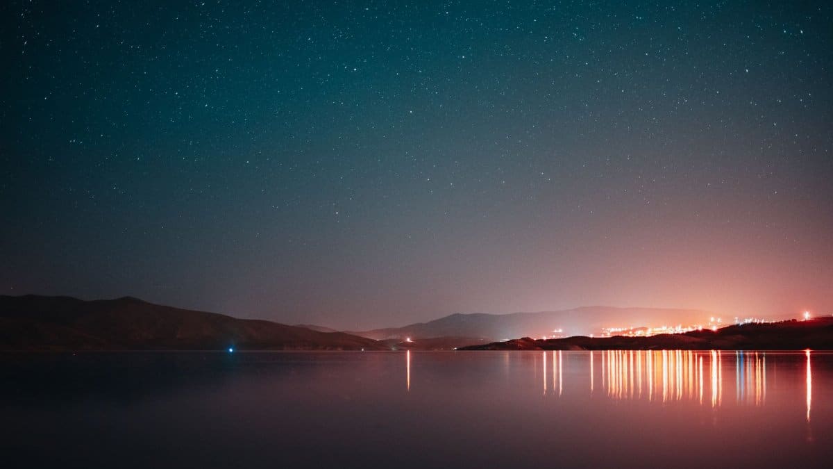 Tranquil nightscape with starry sky and mountain reflections in a serene lake.