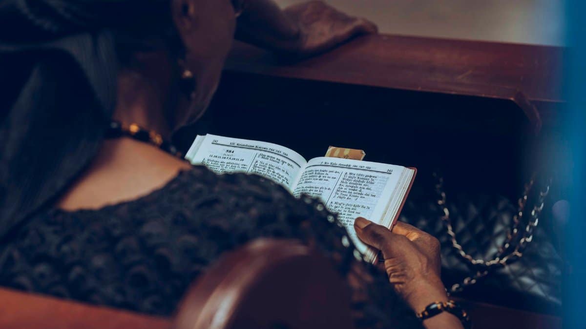A woman reading a prayer book in quiet reflection inside a church.