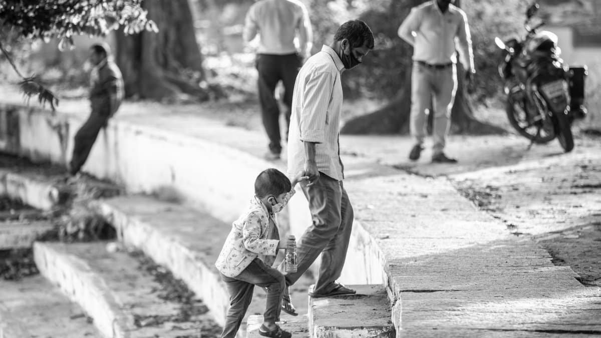 A black and white photo of people wearing masks walking along outdoor stone steps in a park.
