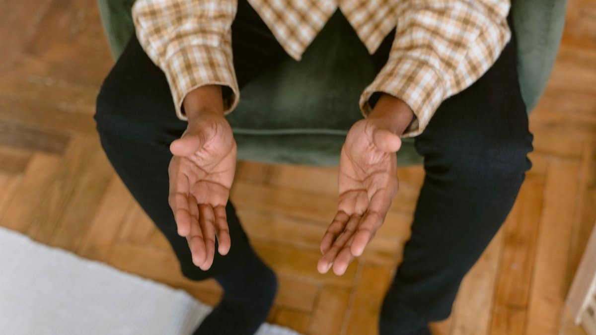 A person sitting indoors with hands open in a reflective prayer pose, inviting tranquility.