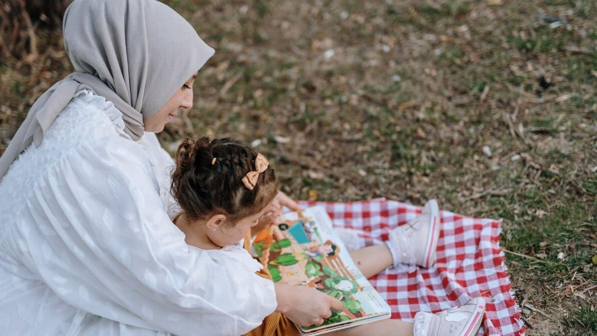 Mother and daughter enjoying a book on a picnic blanket in a park setting.
