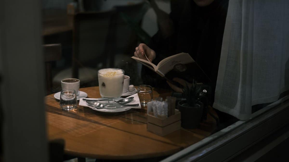 A person enjoys reading a book in a cozy cafe with a warm coffee at night.