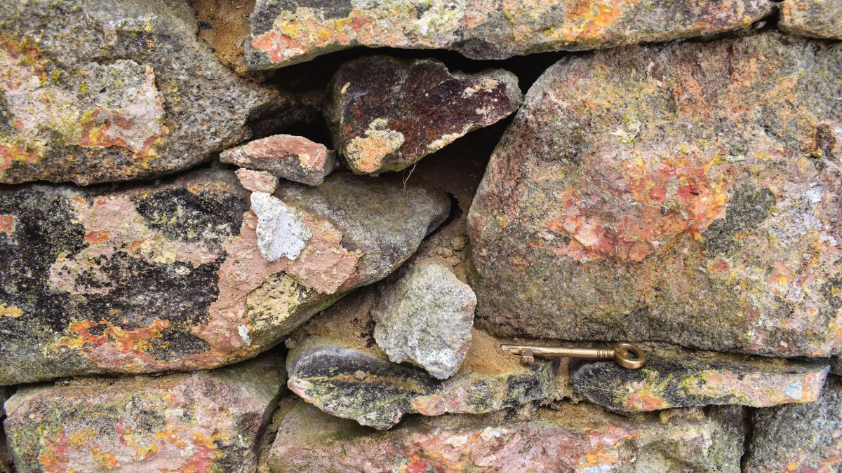 Close-up view of a rustic stone wall with a hidden brass key, showcasing textured and vibrant rock surfaces.