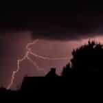A striking lightning bolt illuminates the dark sky over silhouetted houses during a powerful storm.