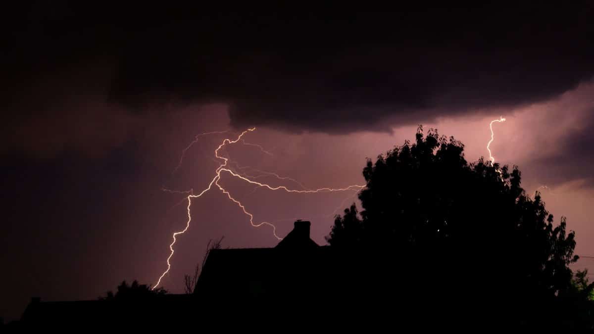A striking lightning bolt illuminates the dark sky over silhouetted houses during a powerful storm.