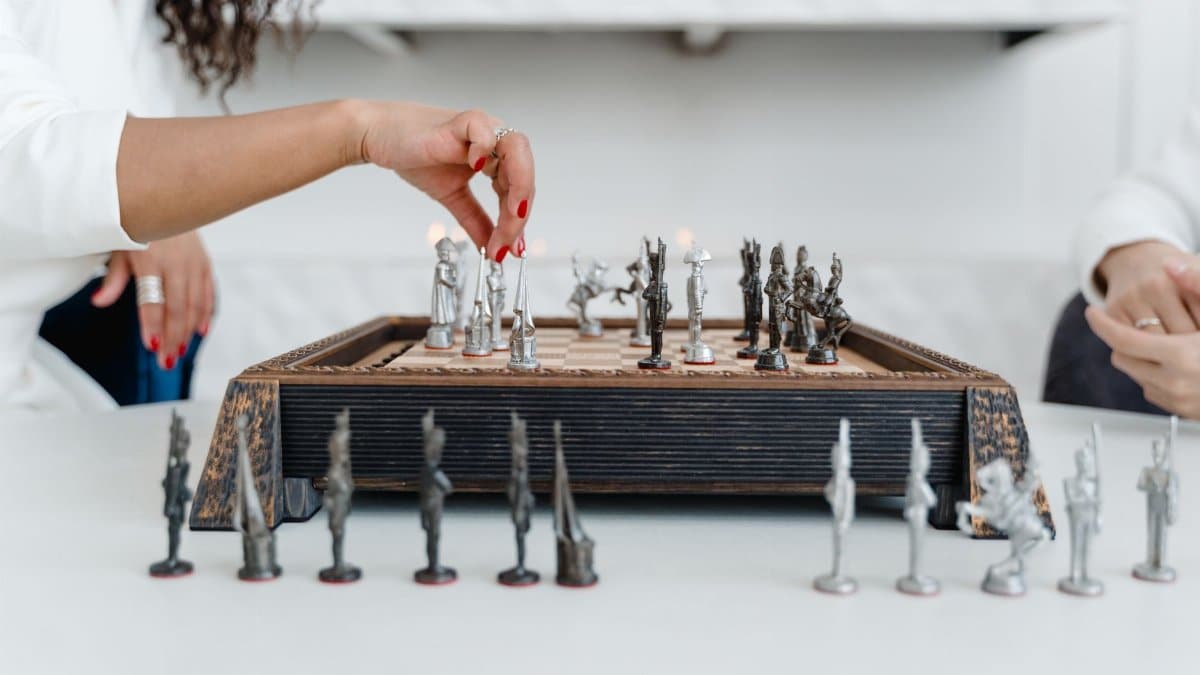 Close-up of hands playing chess on a decorative wooden board, showcasing strategic gameplay.