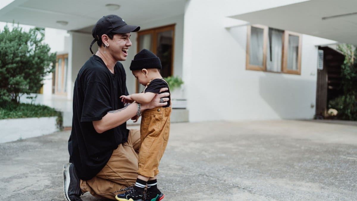 A father and son share a joyful moment outside their home in a vibrant, sunny setting.