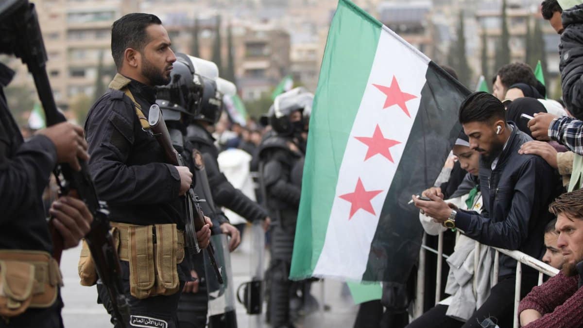 A tense protest scene with security forces and Syrian flags in Damascus, Syria.