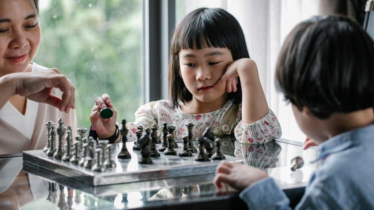 Cheerful Asian grandmother teaching children to play chess while spending time together at home