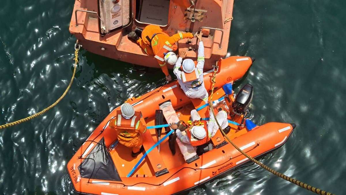 A team conducts a rescue operation on a lifeboat at sea. Captured from above.