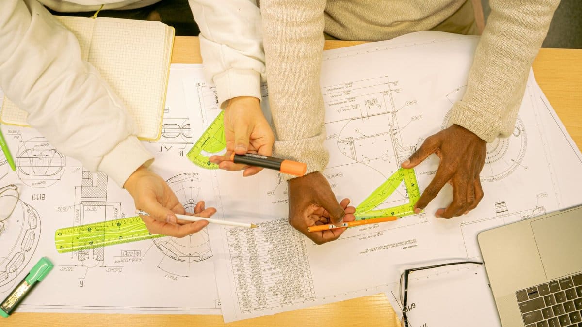 High angle view of architects working on blueprints, using rulers and markers on a wooden table.