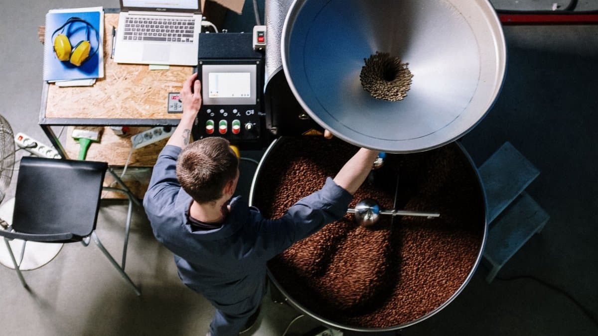 A worker in a coffee roastery operating equipment, processing fresh beans in an industrial setting.