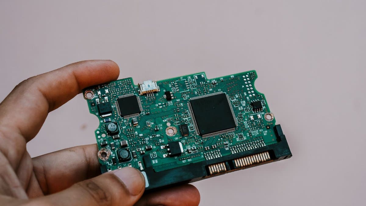 Close-up image of a hand holding a circuit board from a hard drive, showcasing electronic technology.