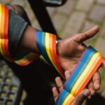 Crop anonymous African American homosexual male wearing colorful rainbow ribbon around arm and sitting on street stairs