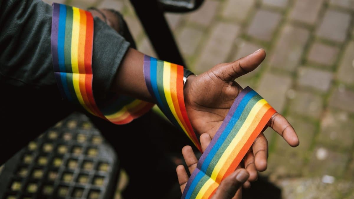 Crop anonymous African American homosexual male wearing colorful rainbow ribbon around arm and sitting on street stairs