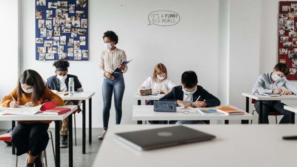 Students and teacher in a classroom wearing masks, embracing new normal education setting.