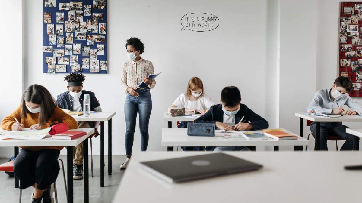 Students and teacher in a classroom wearing masks, embracing new normal education setting.