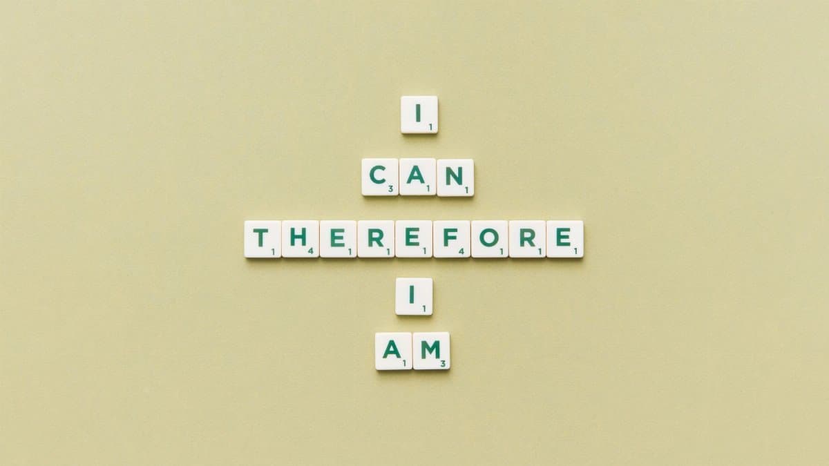 Inspirational phrase 'I Can Therefore I Am' arranged using Scrabble tiles on a green background.