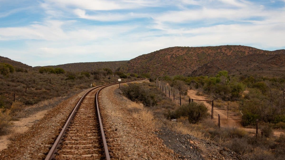 Railway tracks extending through an arid, rural landscape under a vibrant sky.