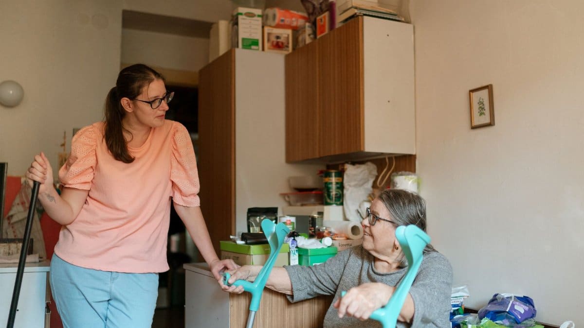 A caregiver engaging with a senior using crutches in a cozy Prague home environment.