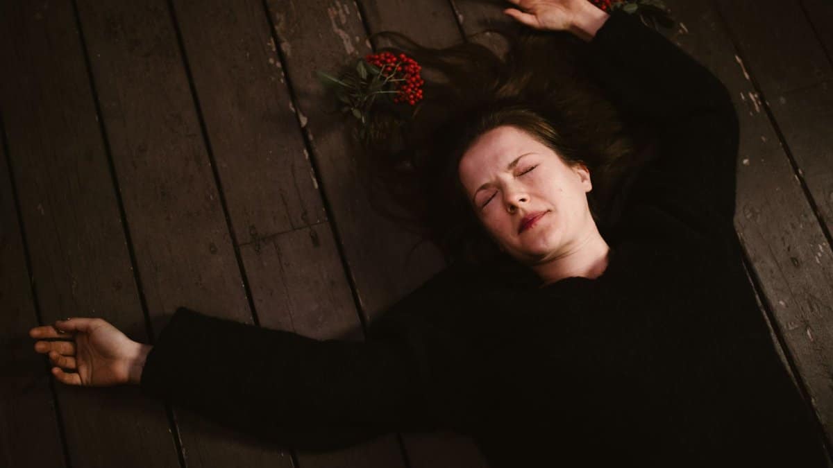 A woman lies on a wooden floor with closed eyes, conveying emotion.