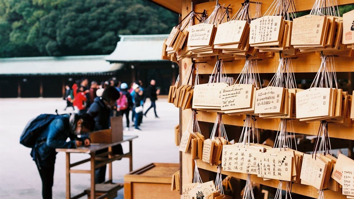 Visitors writing prayers on wooden plaques at a Tokyo shrine, capturing traditional Japanese culture.