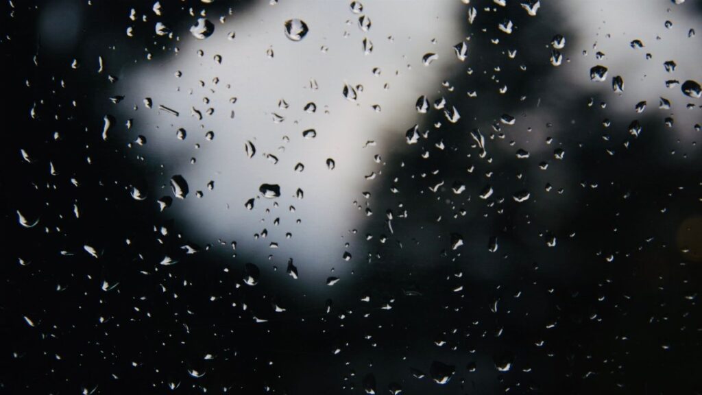 Close-up of rain droplets on a glass window with a dark, blurred background.