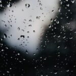 Close-up of rain droplets on a glass window with a dark, blurred background.
