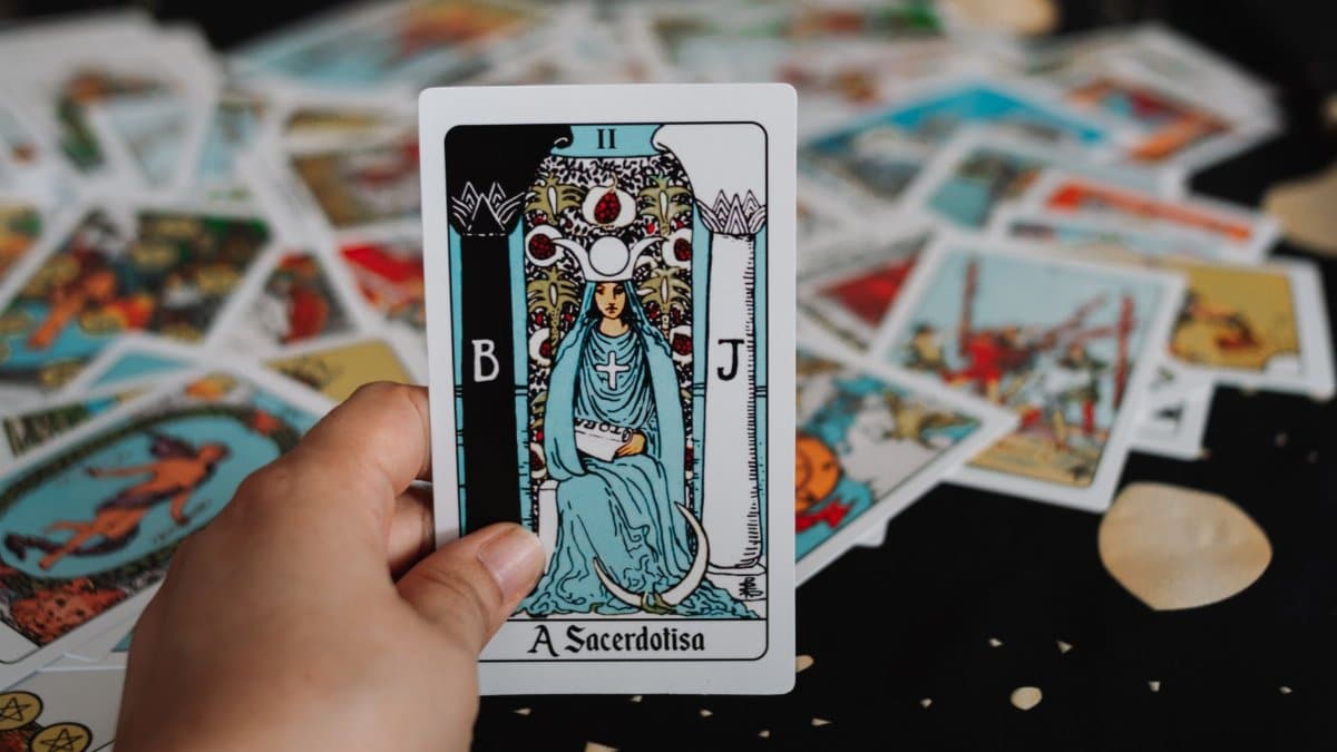 Close-up of a hand holding The High Priestess tarot card among scattered tarot cards.