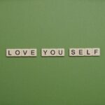 Positive message 'Love You Self' spelled with letter tiles on green background.