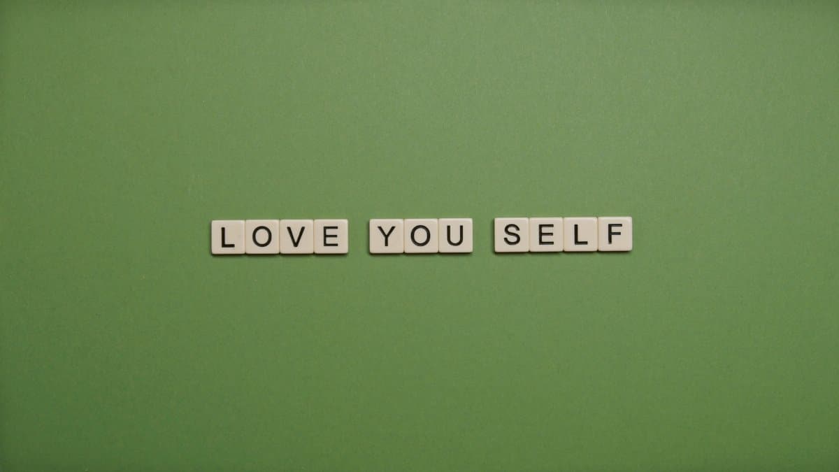 Positive message 'Love You Self' spelled with letter tiles on green background.